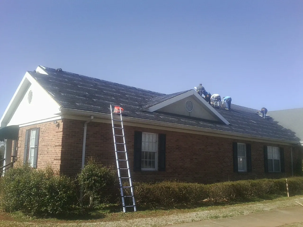 Crew tearing shingles off a brick ranch roof with a ladder set — Emergency Roof Repair work by our crew in Grabill