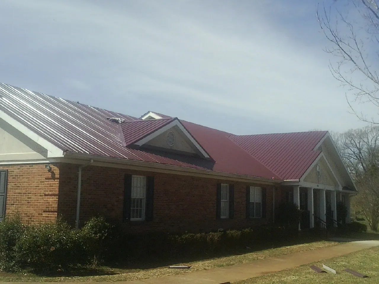 Red metal roof with gabled entries on a long brick building, from a Hail Damage Roof Repair job in Grabill