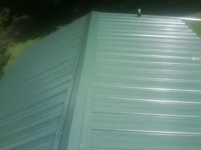New green metal panels meeting at the ridge of a roof — Flat Roof Repair work by our crew in Grabill