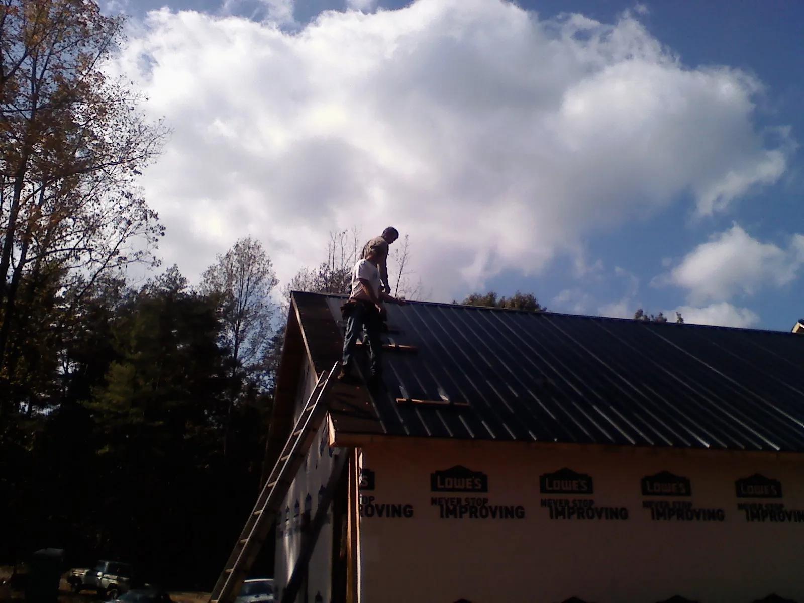 Roofer fastening dark metal panels high against a cloudy sky, from a Roof Inspection job in Grabill