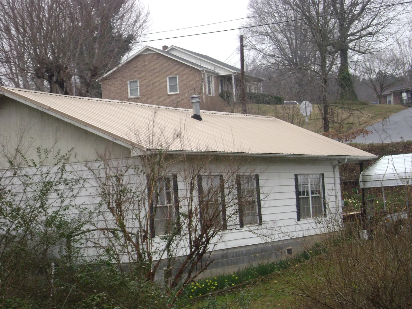 Tan metal roof on a white sided house set into a hillside — Commercial Roofing by Roofing Brothers in Grabill