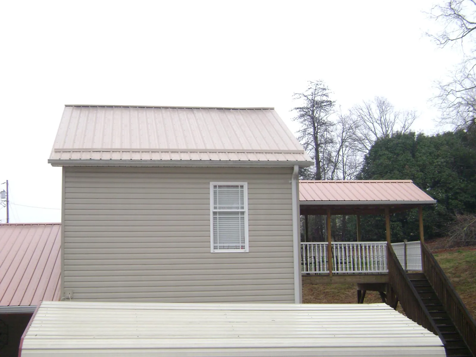Tan metal roofs on a two story addition and attached porch, from a Roof Replacement job in Grabill